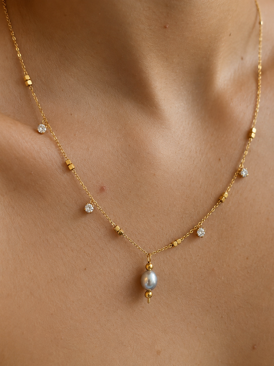 Close-up of a gold necklace with a 6 mm oval grey freshwater pearl and cubic zirconia accents worn on the neck.