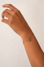 Close-up of a gold double-chain bracelet with a grey baroque freshwater pearl pendant on the wrist
