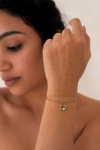Close-up of a petite grey freshwater pearl framed by polished gold beads on a layered gold bracelet