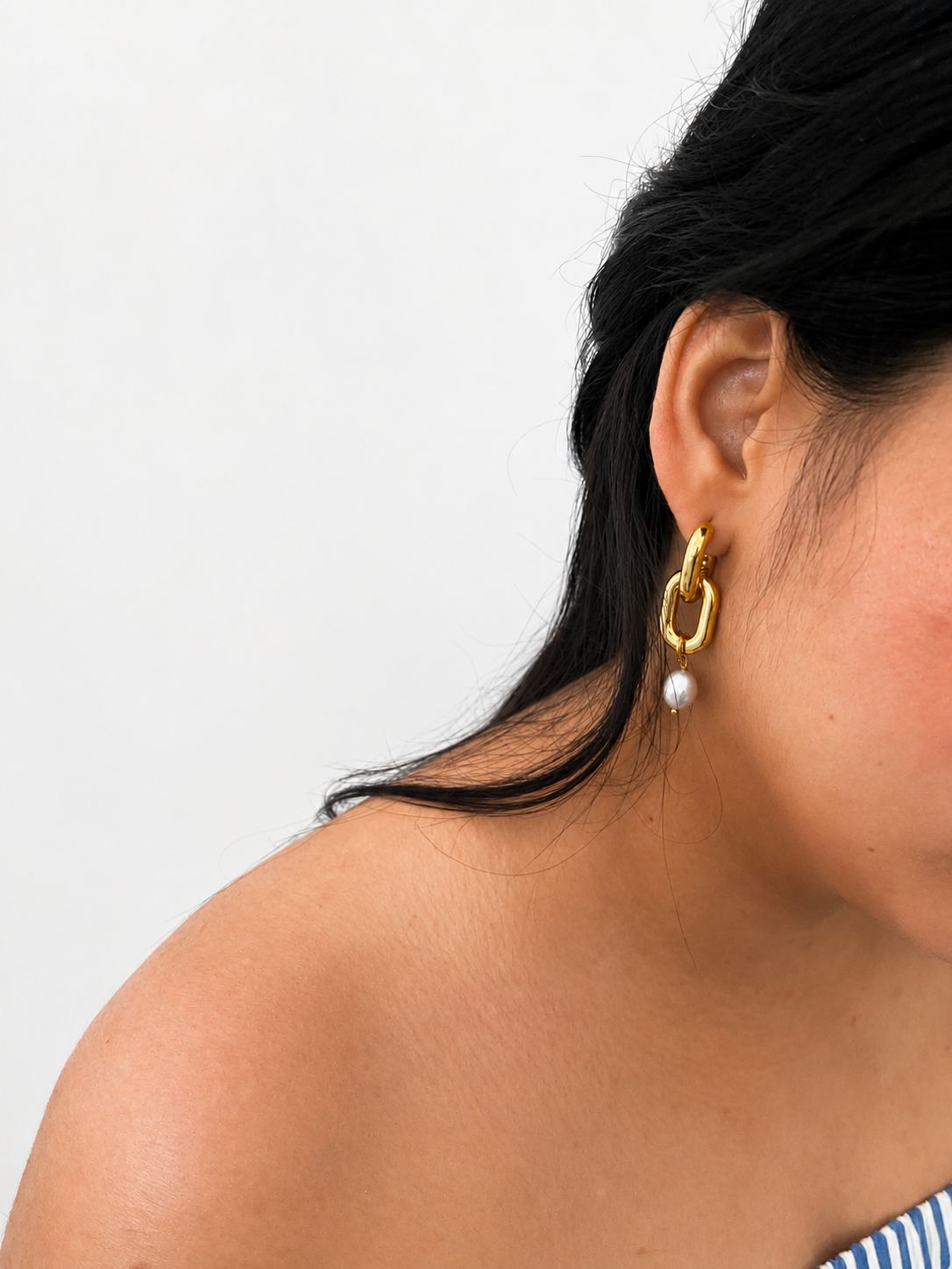 Side view of a gold link drop earring with a grey baroque freshwater pearl worn on the ear.