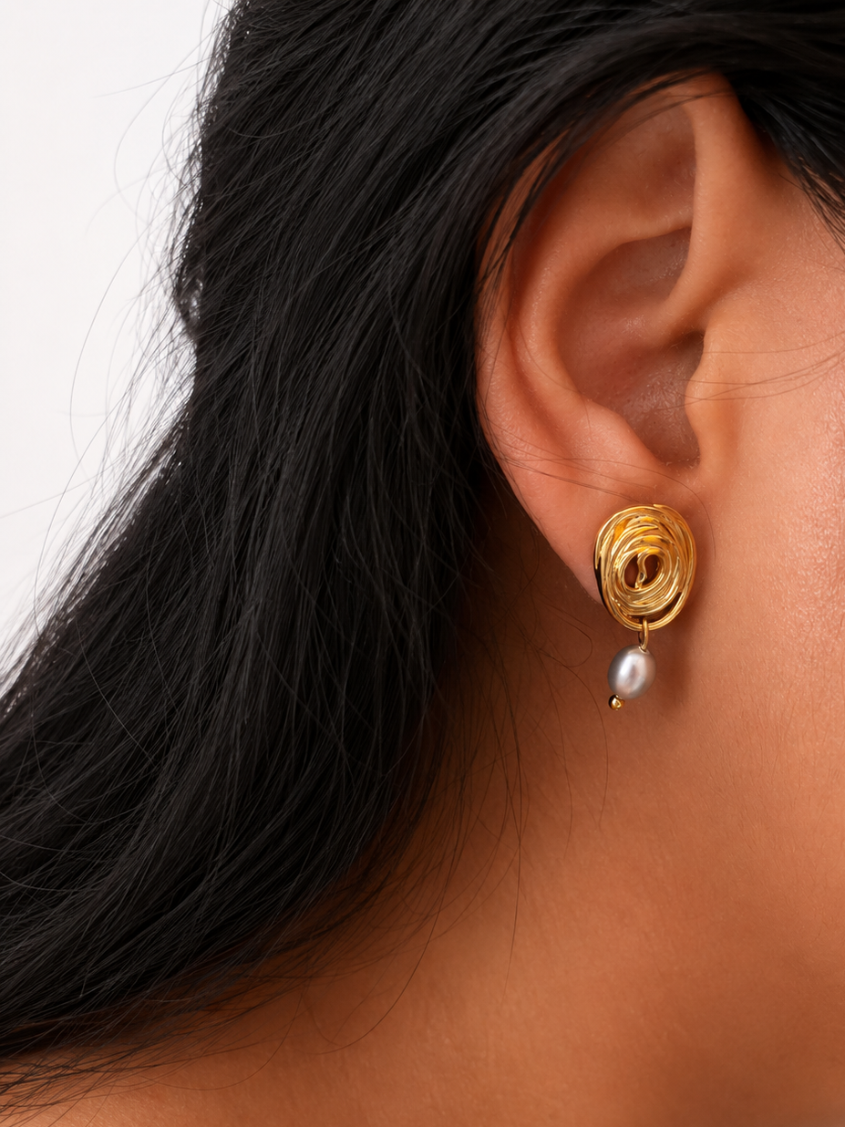 Close-up of a gold spiral stud earring with an oval grey freshwater pearl drop worn on the ear.