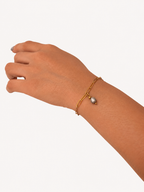Grey pearl drop bracelet with a gold paperclip-link chain worn on the wrist