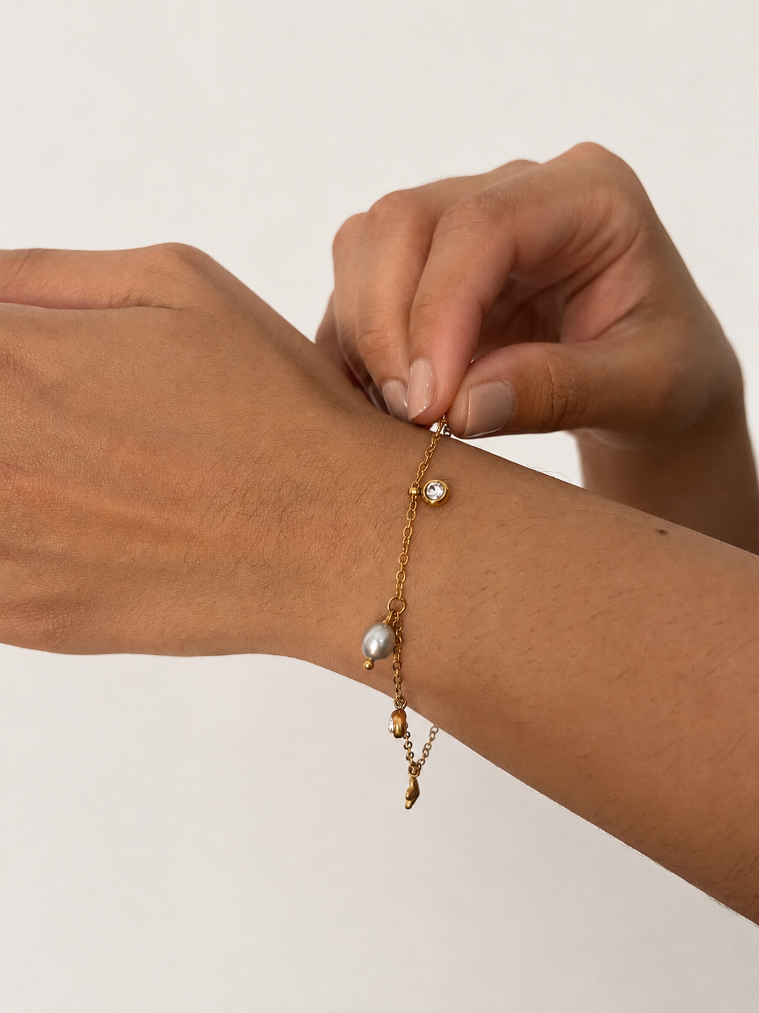 Close-up of a grey pearl and clear stone charm bracelet being adjusted on the wrist