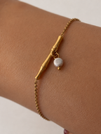 Close-up of a gold twig bar bracelet with a small grey pearl charm and polished gold bead