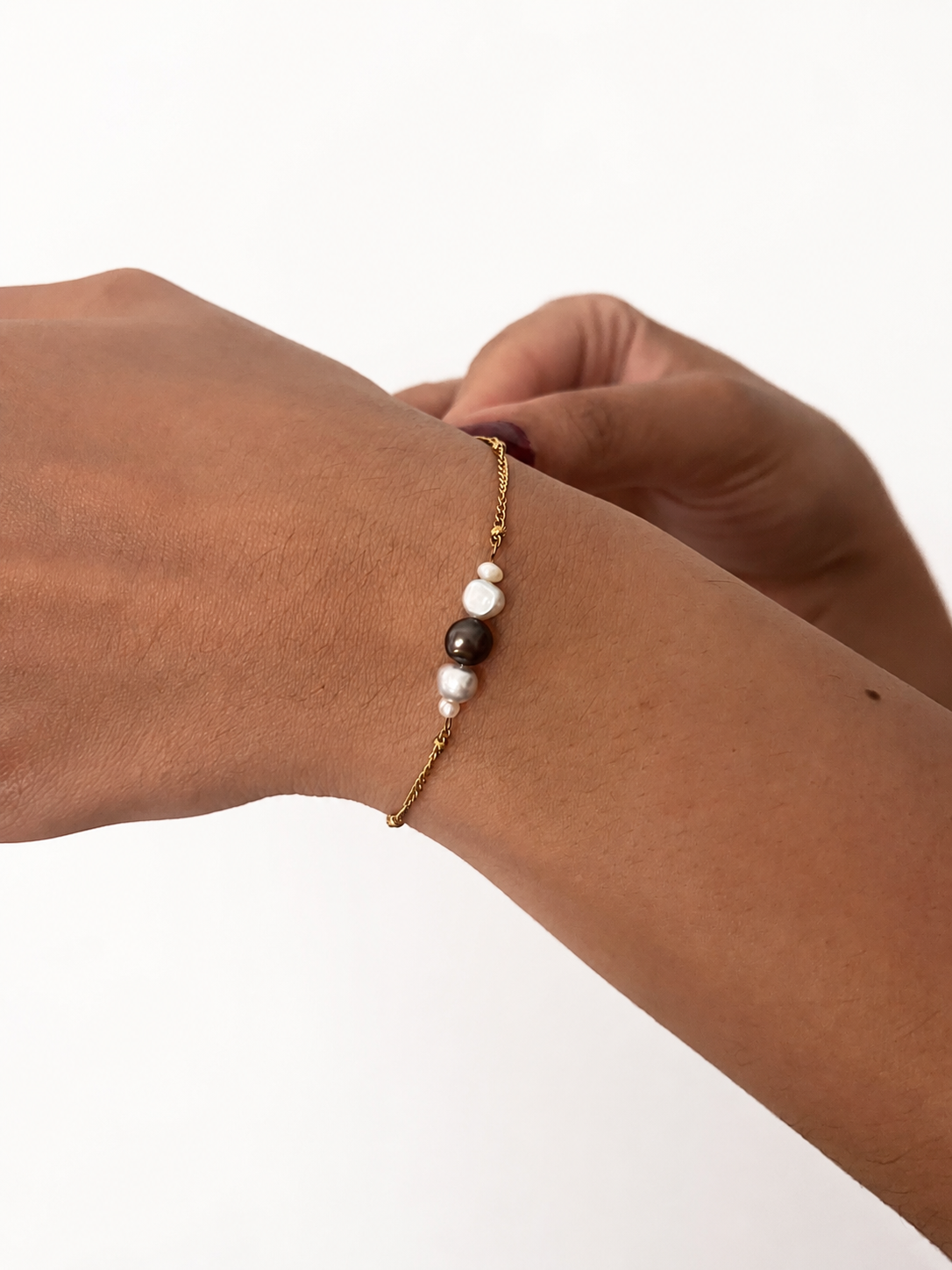 Close-up of a delicate gold bracelet with a grey centre pearl and small white pearls on the wrist