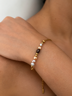 Close-up of a gold chain bracelet with a dark grey pearl, white and champagne pearls, and polished gold beads