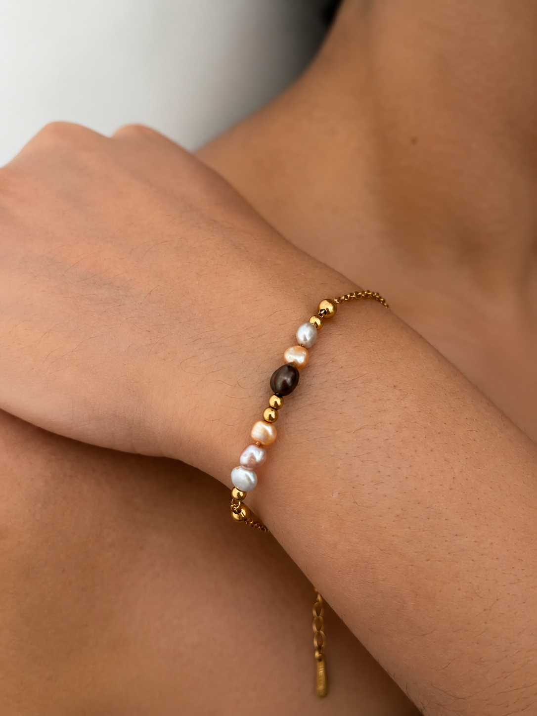 Close-up of a gold chain bracelet with a dark grey pearl, white and champagne pearls, and polished gold beads