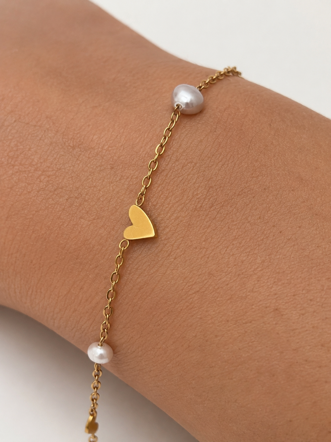 Close-up of a gold heart bracelet with a grey baroque pearl and petite white pearl on the wrist