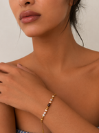 Woman wearing a delicate gold chain bracelet with grey, white and champagne-toned pearls