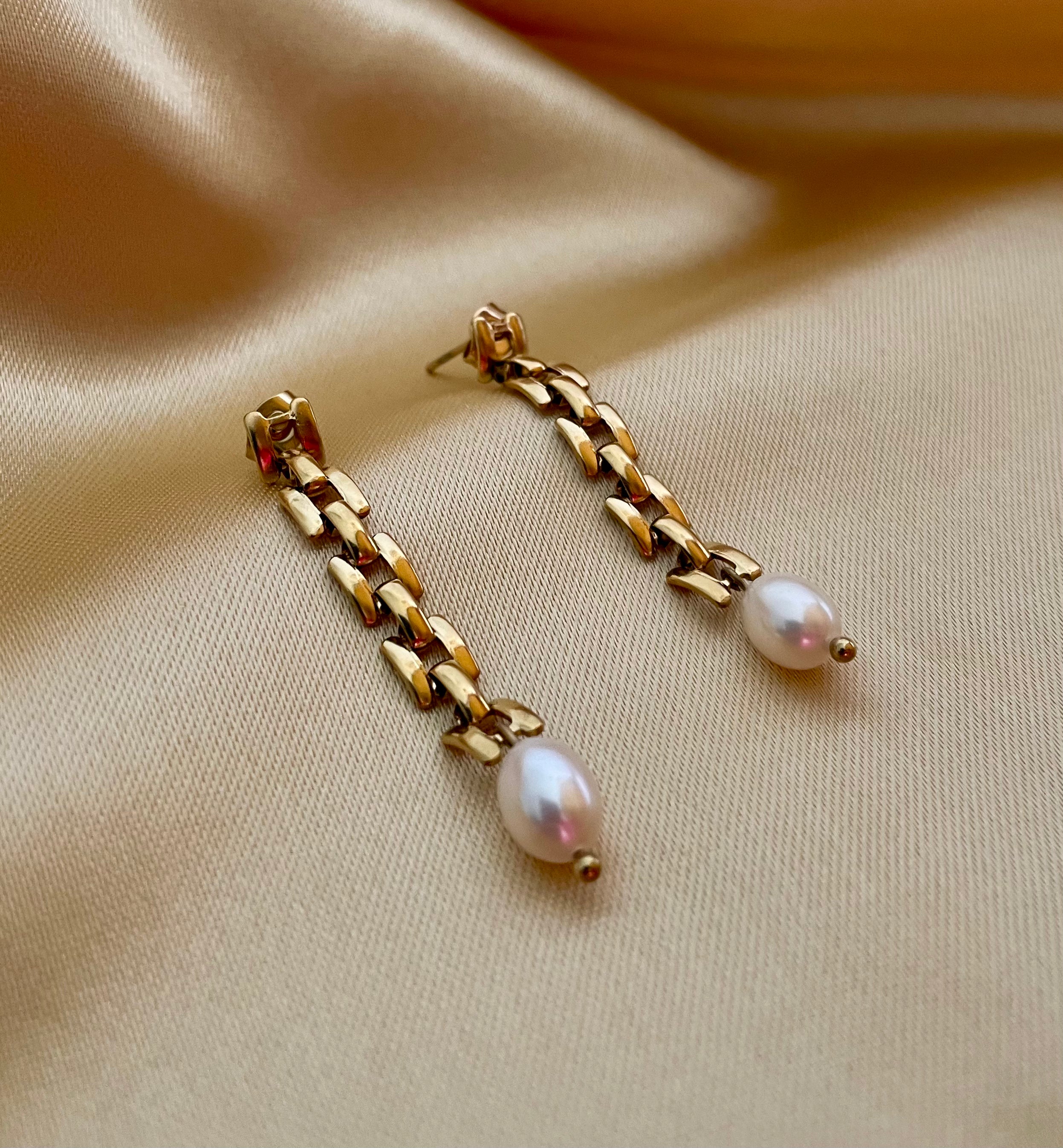 Close-up detail showing the high luster of a white oval pearl and the vintage-style gold link chain connection. Luxury jewelry design