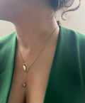 Gold necklace with a pendant worn by a person in a green outfit.