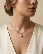 Grey baroque pearl necklace on layered gold chains. High-quality jewelry photography showing the metallic iridescence of the pearl and fine texture of the gold links on a model's neck