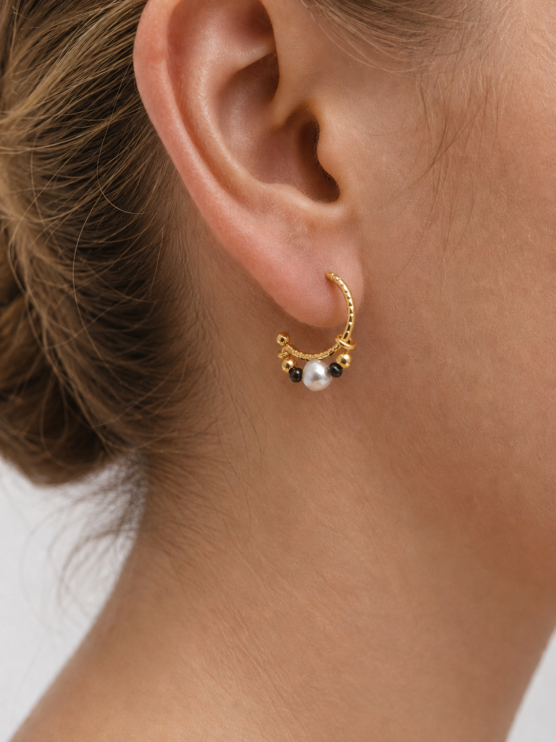 Woman wearing a gold creole hoop earring with a 4 mm light grey baroque pearl and 2 mm dark grey Keshi pearls