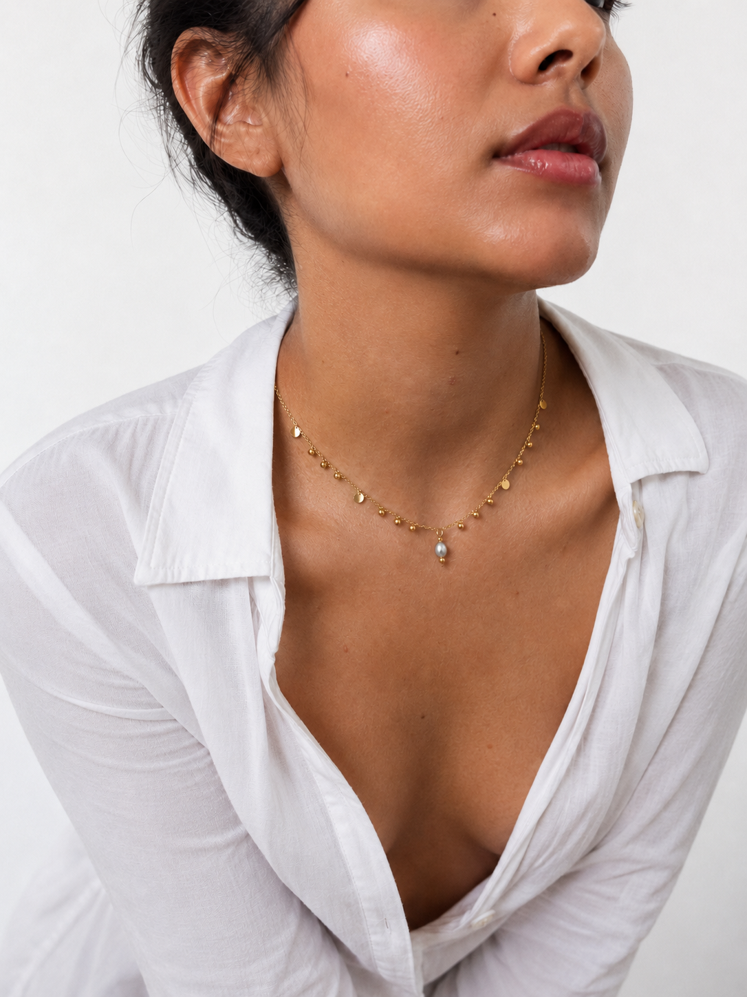 Woman wearing a gold bead charms necklace with polished disc accents and a light grey freshwater pearl pendant
