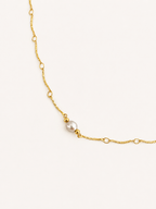 Close-up of a textured gold Waves necklace with a light grey freshwater pearl and polished gold bead accents