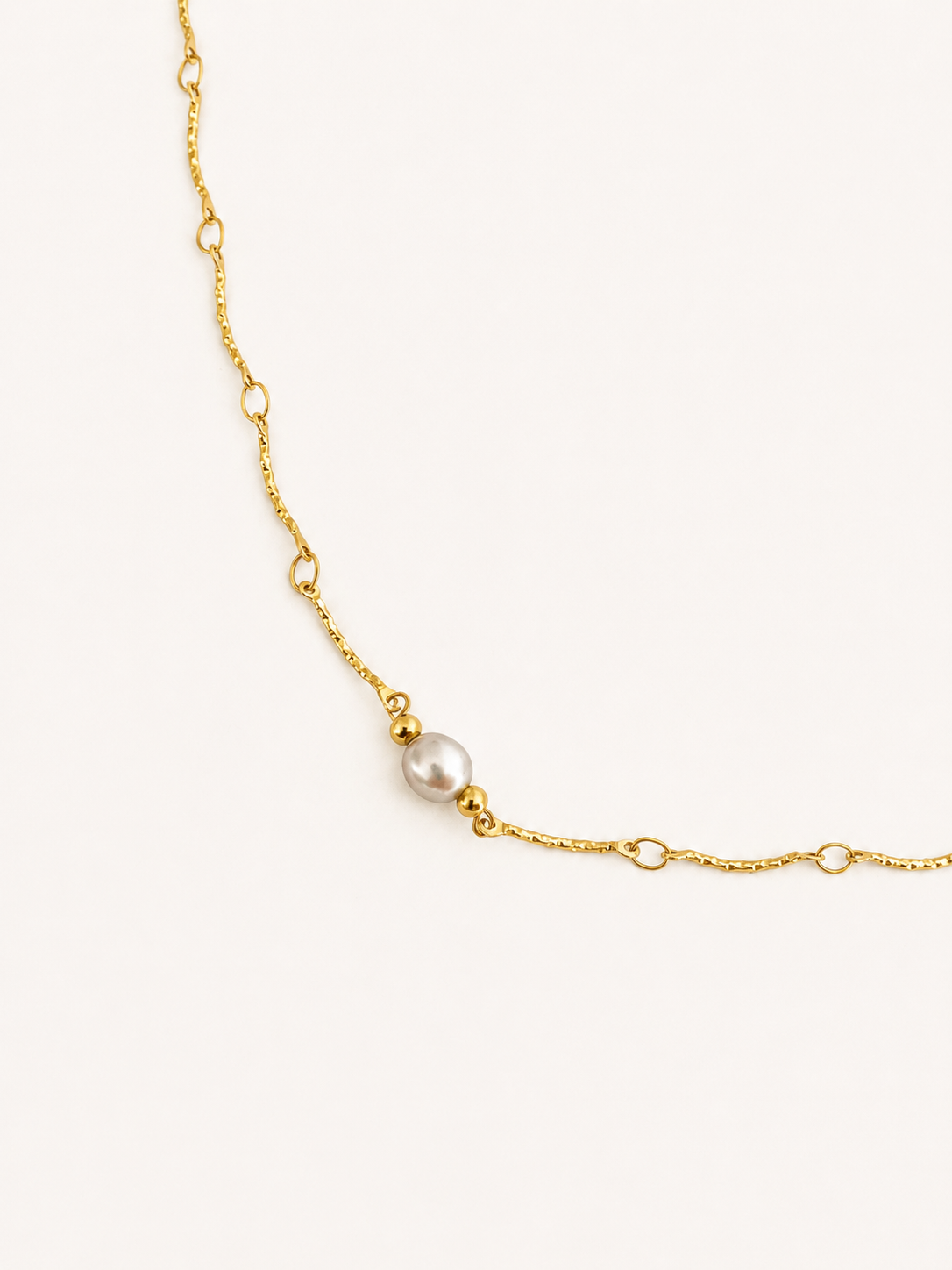Close-up of a textured gold Waves necklace with a light grey freshwater pearl and polished gold bead accents