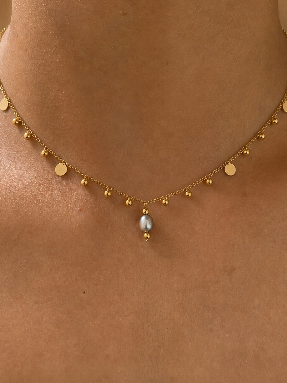 Close-up of a gold bead charms necklace with a 6 mm oval light grey freshwater pearl worn on the neck