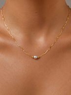 Close-up of a gold Waves necklace with a 6 mm oval light grey freshwater pearl worn on the neck