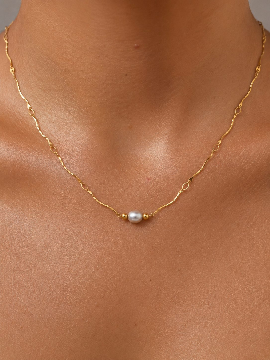 Close-up of a gold Waves necklace with a 6 mm oval light grey freshwater pearl worn on the neck