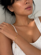 Woman wearing a delicate gold heart bracelet with grey and white freshwater pearls and a white dress