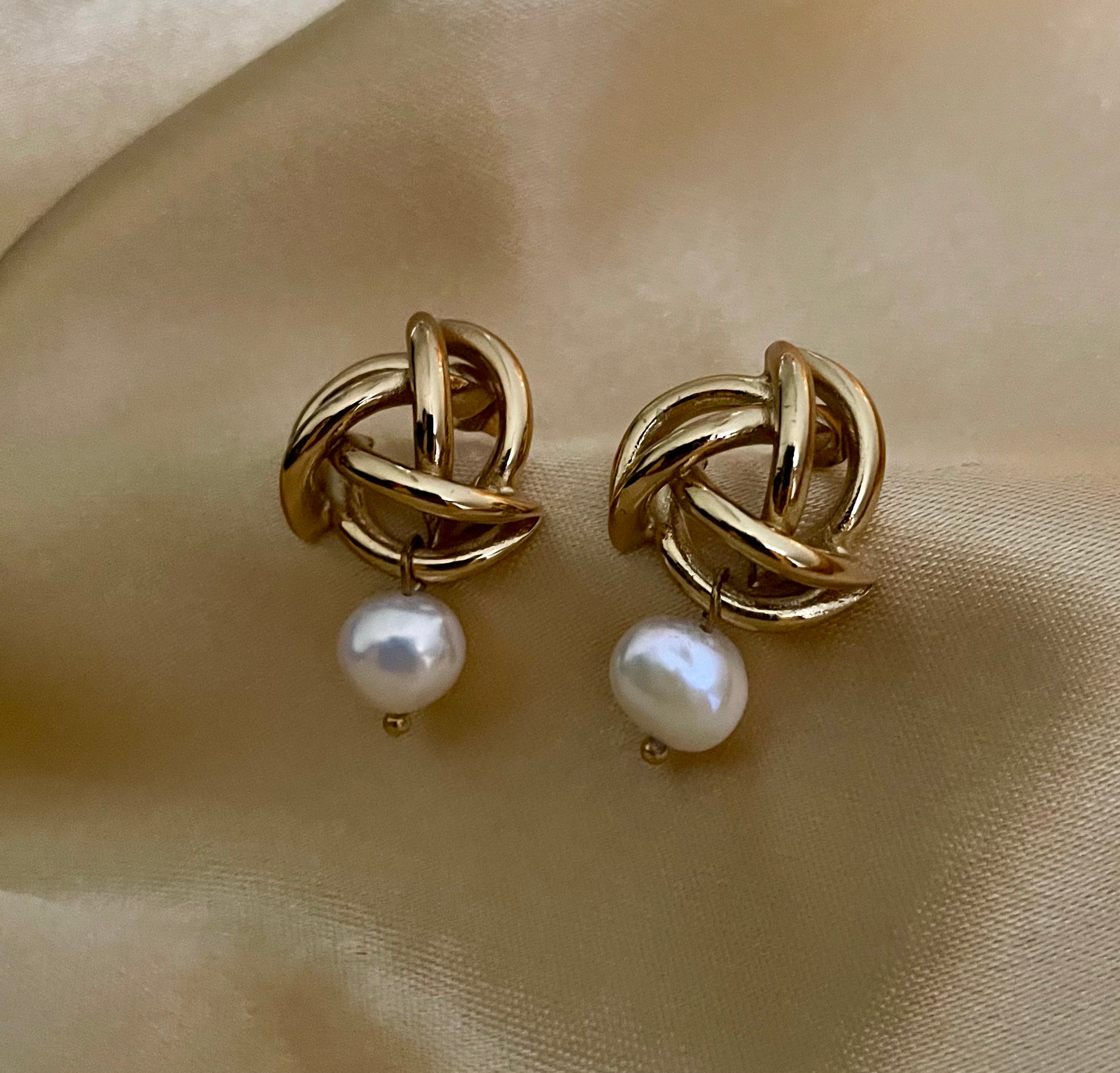 Close-up of gold twisted knot earrings with a white pearl drop