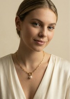 Elegant jewelry photography close-up showing a chunky gold link necklace with a pearl drop, worn by a model with a deep-neck silk blouse.