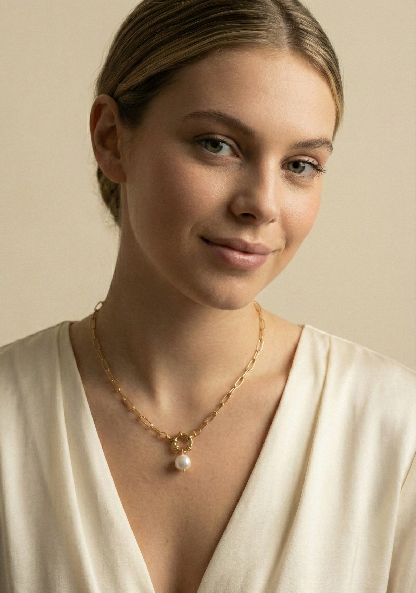 Elegant jewelry photography close-up showing a chunky gold link necklace with a pearl drop, worn by a model with a deep-neck silk blouse.