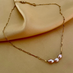High-resolution jewelry photography showing the detailed luster of three pink oval pearls on a fine gold link chain, draped elegantly on a model's collarbone for a luxury commercial aesthetic