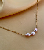 delicate gold chain necklace featuring three small, oval pink pearls with a high silvery luster