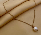 Minimalist fine jewelry styling showing a single freshwater pearl drop necklace on a delicate gold beaded chain, highlighting the high-luster nacre and skin texture