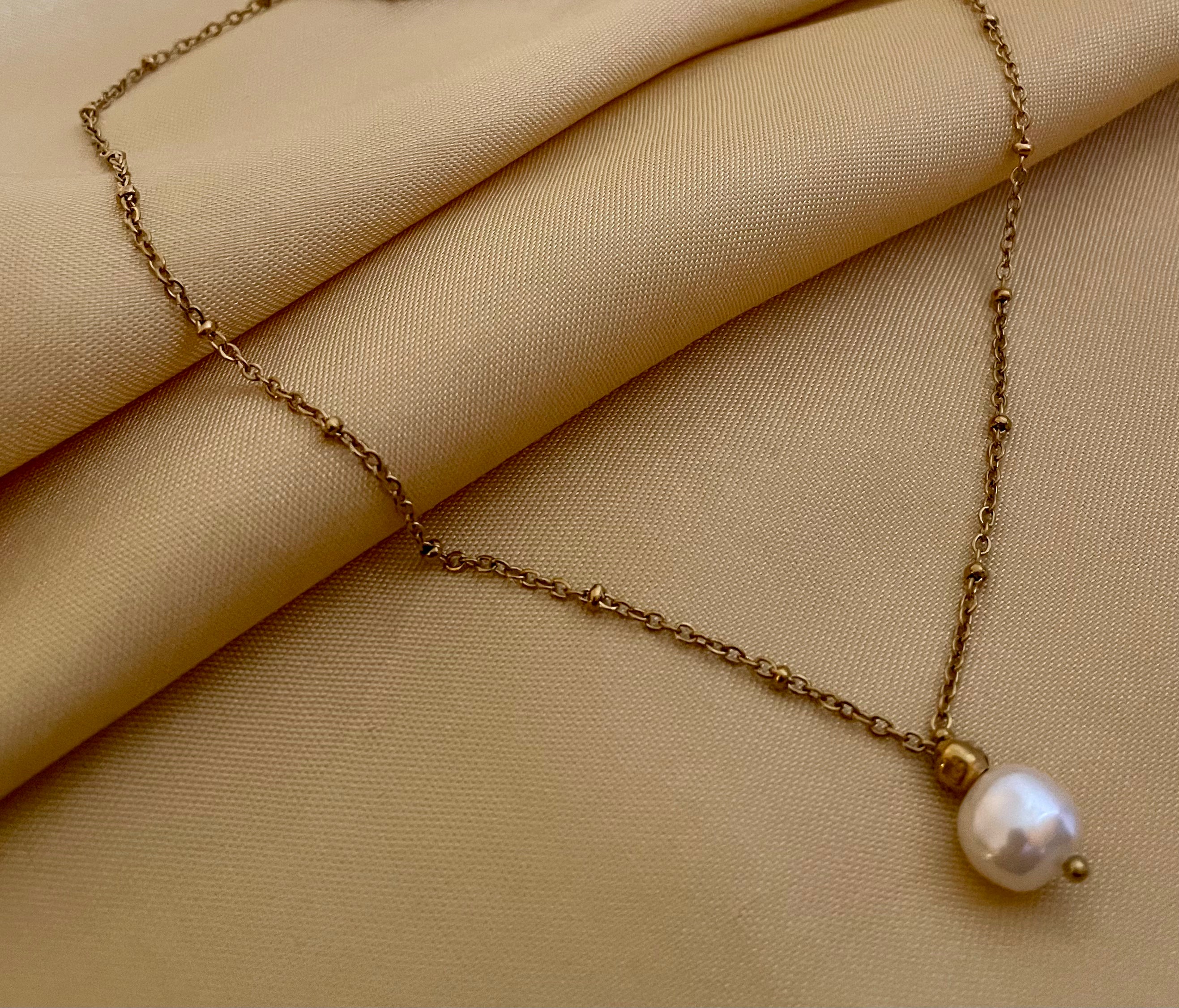 Minimalist fine jewelry styling showing a single freshwater pearl drop necklace on a delicate gold beaded chain, highlighting the high-luster nacre and skin texture