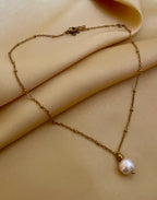 Minimalist fine jewelry styling showing a single freshwater pearl drop necklace on a delicate gold beaded chain, highlighting the high-luster nacre and skin texture