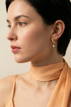 Woman wearing minimalist yellow gold hoop earrings with a small, organic grey pearl dangle.