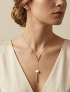 Woman wearing an elegant deep-neck cream top styled with a modern gold bar lariat necklace and a lustrous pearl pendant