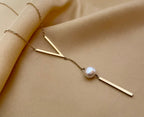 Close-up of a gold lariat necklace featuring a geometric V-shaped bar and a single white baroque pearl drop on a delicate chain