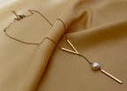 Close-up of a gold lariat necklace featuring a geometric V-shaped bar and a single white baroque pearl drop on a delicate chain