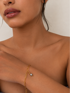 Woman wearing a minimalist gold paperclip-chain bracelet with a grey pearl drop
