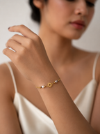 Woman styling a minimalist gold sun bracelet with small grey freshwater pearls and a white satin top