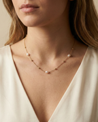 Close-up of a dainty gold chain necklace featuring three small, oval champagne pearls and gold spacer beads, worn by a model in an ivory silk top