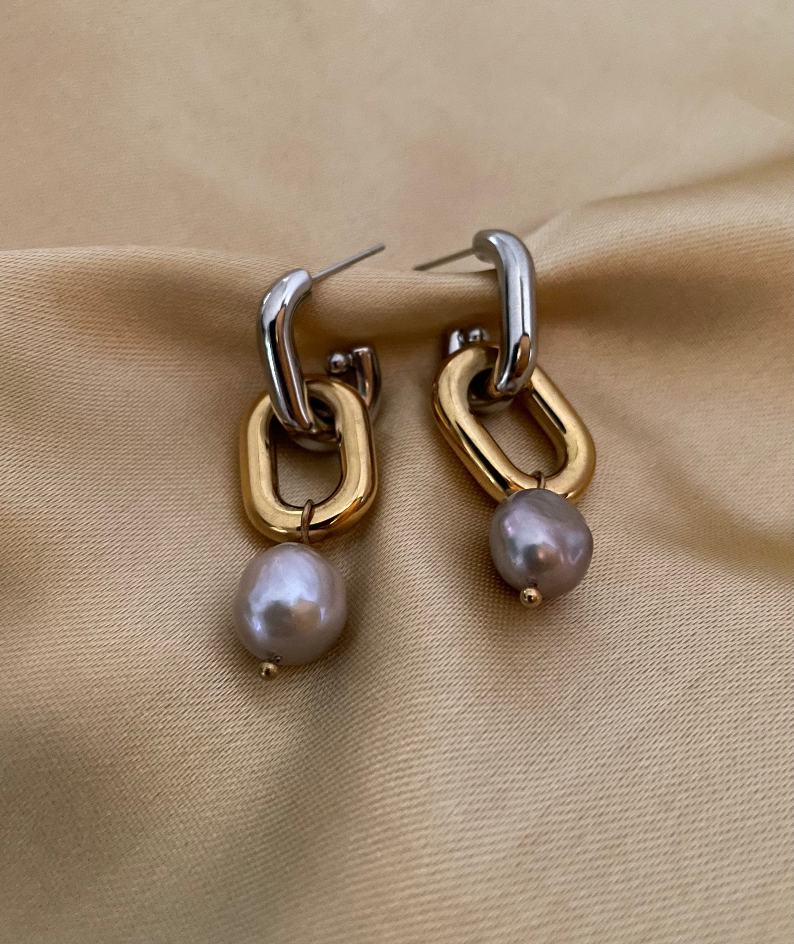 Close-up detail of mixed metal chain link earrings with grey pearl drops worn on the ear.