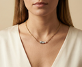 Close-up editorial portrait of a woman wearing a gold oval-link chain necklace featuring a grey baroque keshi pearl and a small white pearl, styled with a deep V-neck ivory silk top