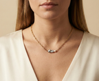 Close-up editorial portrait of a woman wearing a gold oval-link chain necklace featuring a grey baroque keshi pearl and a small white pearl, styled with a deep V-neck ivory silk top