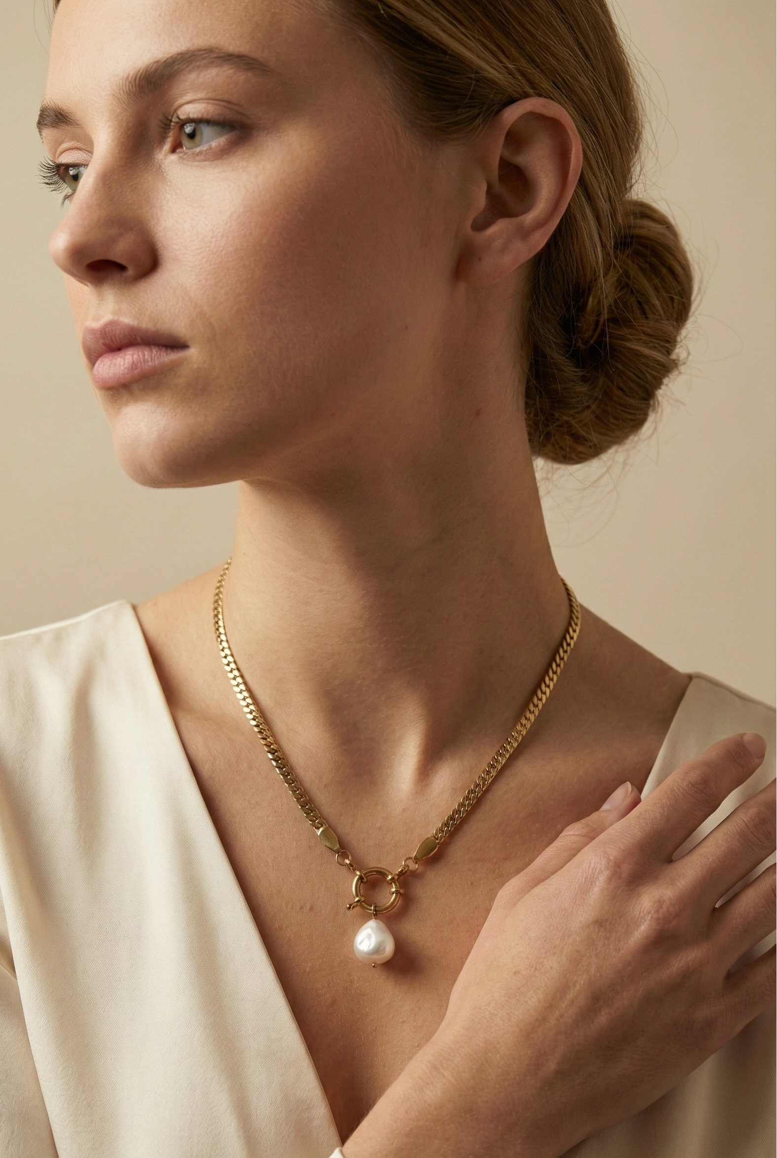 Model wearing an elegant gold chain necklace with a white baroque pearl drop and front clasp detail, styled with an ivory silk V-neck top