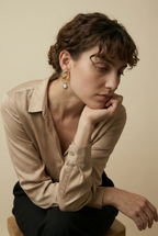 Elegant model wearing modern artisan gold earrings with an irregular organic shape and hanging grey pearl pendant, styled with an ivory silk scarf in soft natural lighting