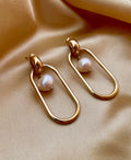 Editorial shot of a modern geometric gold hoop earrings with a floating freshwater baroque pearl center, set against a warm beige background