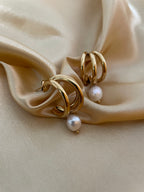 Macro detail of high-luster white pearl charm attached to a polished gold triple-row hoop earring