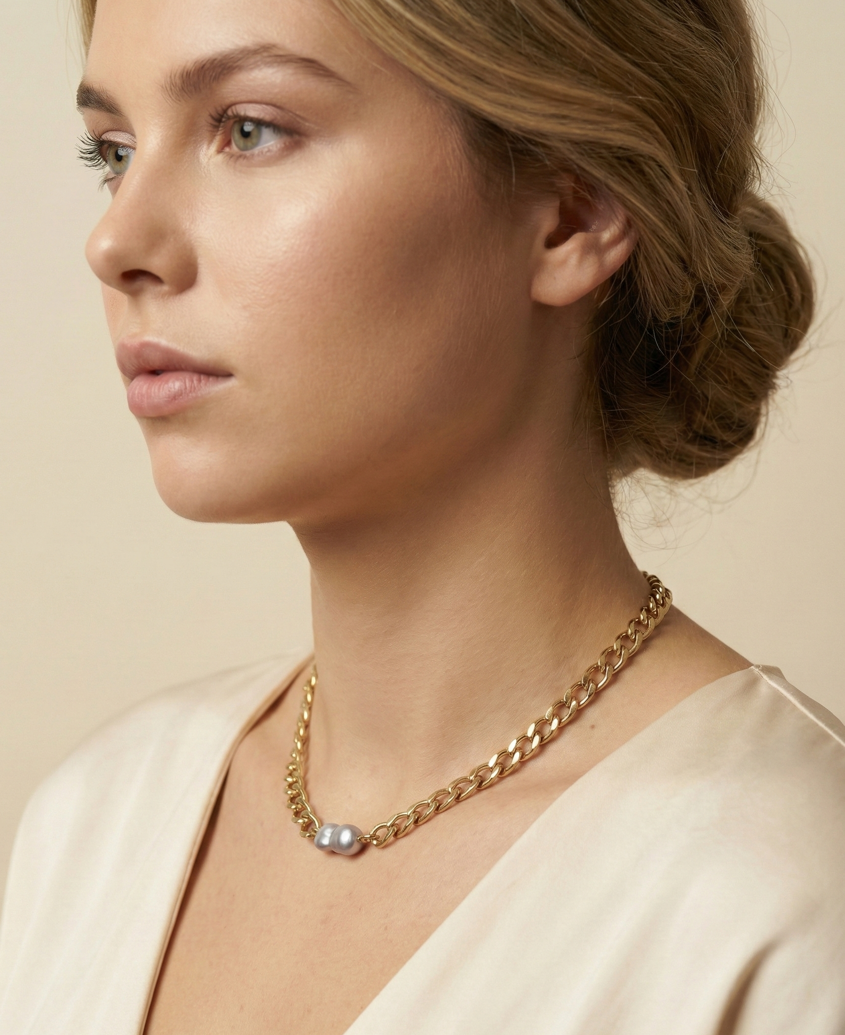 Elegant model wearing a modern gold chain necklace with a single organic grey pearl pendant, showcasing a minimalist luxury jewelry style against a cream silk top.