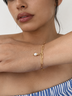 Woman wearing a gold paperclip-link bracelet with a white freshwater pearl drop and polished gold beads