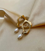 Close-up detail of organic-shaped gold drop earrings featuring a small white oval pearl