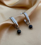 Close-up detail of AAA quality round black freshwater pearl on PVD 18k gold plated stainless steel drop earrings. High-lustre dark pearl texture.